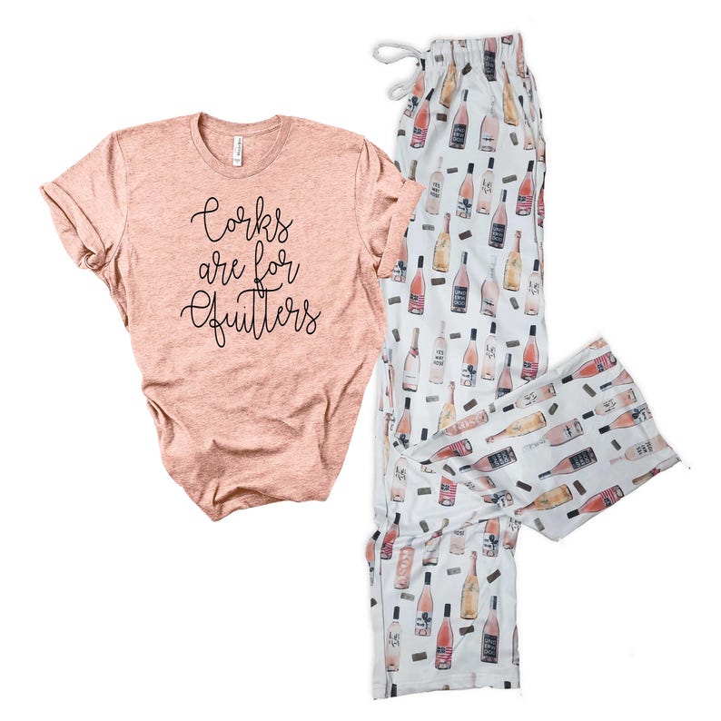 May include: A pink t-shirt with the text "Corks are for quitters" and white pajama pants with a pink wine bottle print.