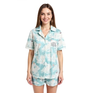 May include: A light blue and white pajama set with a cloud pattern. The short-sleeved top has a button-down front and a pocket with embroidered initials. The matching shorts have a white trim.
