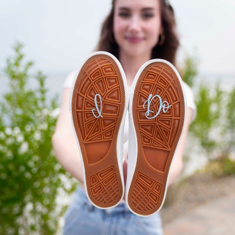 May include: A pair of white canvas shoes with the words "I Do" and "I" written on the soles.