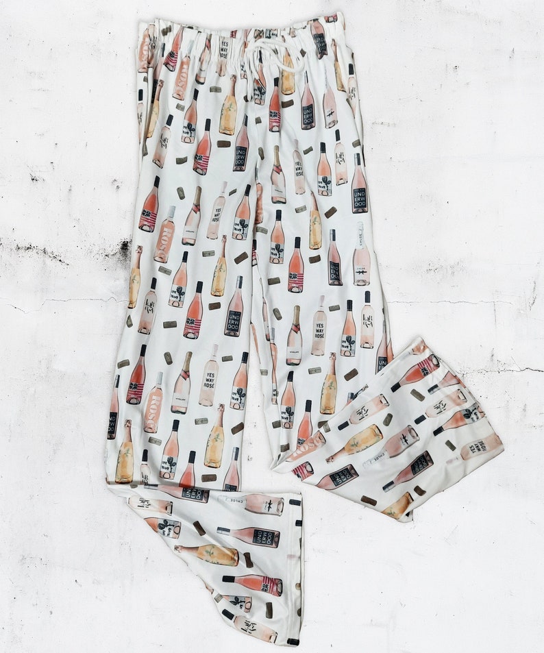 May include: White pajama pants with a pink wine bottle print. The bottles are illustrated with various labels and corks.