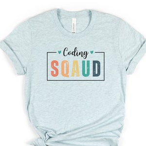 May include: A light blue t-shirt with the text "Coding Squad" in a colorful retro font. The text is enclosed in a black rectangle with a small heart on either side.
