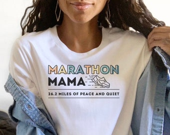 Puede incluir: Camiseta blanca con el texto "Marathon Mama" en colores arcoíris y un gráfico de una zapatilla para correr. El texto debajo del gráfico dice "26.2 millas de paz y tranquilidad".