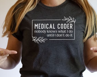 May include: A dark grey heather t-shirt with the text "MEDICAL CODER nobody knows what I do until I don't do it" in a white rectangle with a floral design. The text "DARK GREY HEATHER" and the logo "Smarty Pants Studio" are also visible.