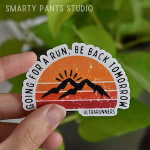 May include: A white sticker with a retro sunset design featuring mountains and the text "Going for a run, be back tomorrow - Ultrarunners".
