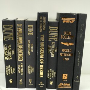 May include: A collection of black hardcover books with gold lettering. The titles include "Dune", "The Machine Crusade", "Captain's Blood", "House Harkonnen", "The Museum of Desire", "The Butlerian Jihad", "World Without End", and "Disobedience".
