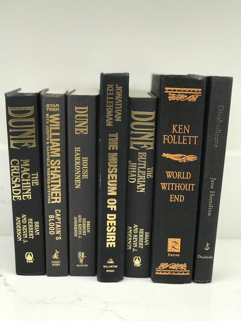 May include: A collection of black hardcover books with gold lettering. The titles include "Dune", "The Machine Crusade", "Captain's Blood", "House Harkonnen", "The Museum of Desire", "The Butlerian Jihad", "World Without End", and "Disobedience".