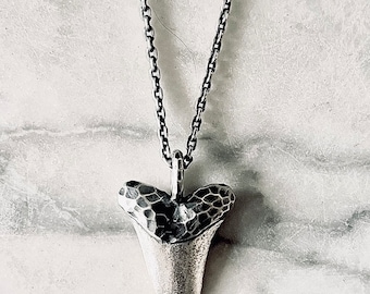 May include: A silver chain necklace with a hammered silver shark tooth pendant.