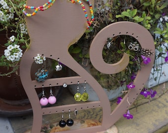 Pode incluir: Um suporte de brincos de madeira em forma de gato com um design floral na base. O suporte tem várias ranhuras para brincos e um suporte para colares na cabeça. O gato é pintado de cor castanho claro com detalhes dourados.