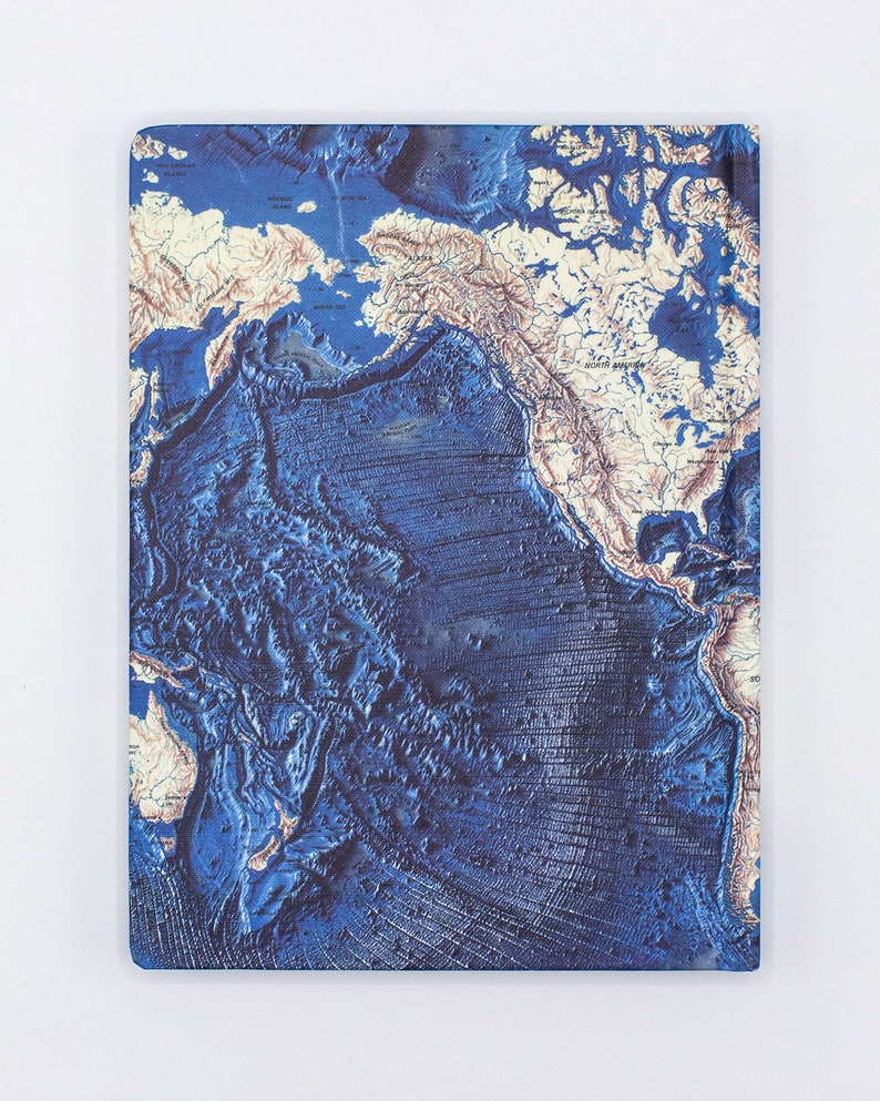 Puede incluir: Un cuaderno azul y blanco con un mapa del mundo con un dise&ntilde;o texturizado en 3D. El mapa muestra la topograf&iacute;a del fondo del oc&eacute;ano con tonos azules profundos y colores azul claro y blanco para las masas terrestres.