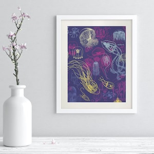 May include: A framed art print featuring a detailed illustration of various jellyfish in shades of yellow, blue, and pink on a dark purple background. The artwork is displayed in a white frame and is part of a home decor collection.