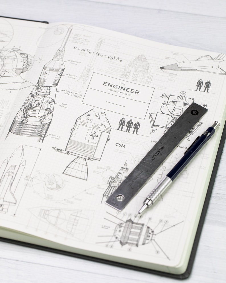 May include: An open notebook featuring detailed diagrams of rockets and spacecraft. A metal ruler and a pen are placed on the open pages. The cover reads "ENGINEER NOTEBOOK SERIES". The pages are white with black ink.