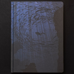 May include: A blue notebook with a design of a diver swimming through a school of fish in a dark blue ocean. The design is printed on the cover of the notebook.