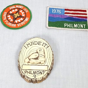 May include: Three vintage Philmont memorabilia items. Includes a round patch with "South Florida Scouting" and "Philmont 1976". A rectangular patch with a flag design and "Philmont 1976". A wooden plaque with "I MADE IT!" and a boot illustration.