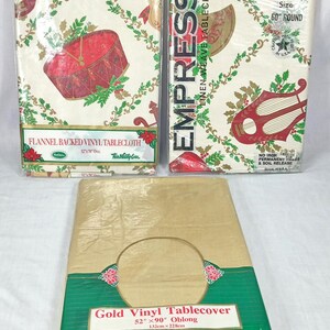 May include: Three packaged vinyl tablecloths. Two are white with a Christmas design featuring a drum and a harp. The third is gold with a green border. The gold tablecloth is 52" x 90" (132cm x 228cm).