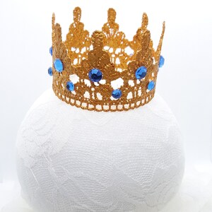 Peut inclure: Une couronne dor&eacute;e avec des pierres bleues, en dentelle, sur un fond blanc.