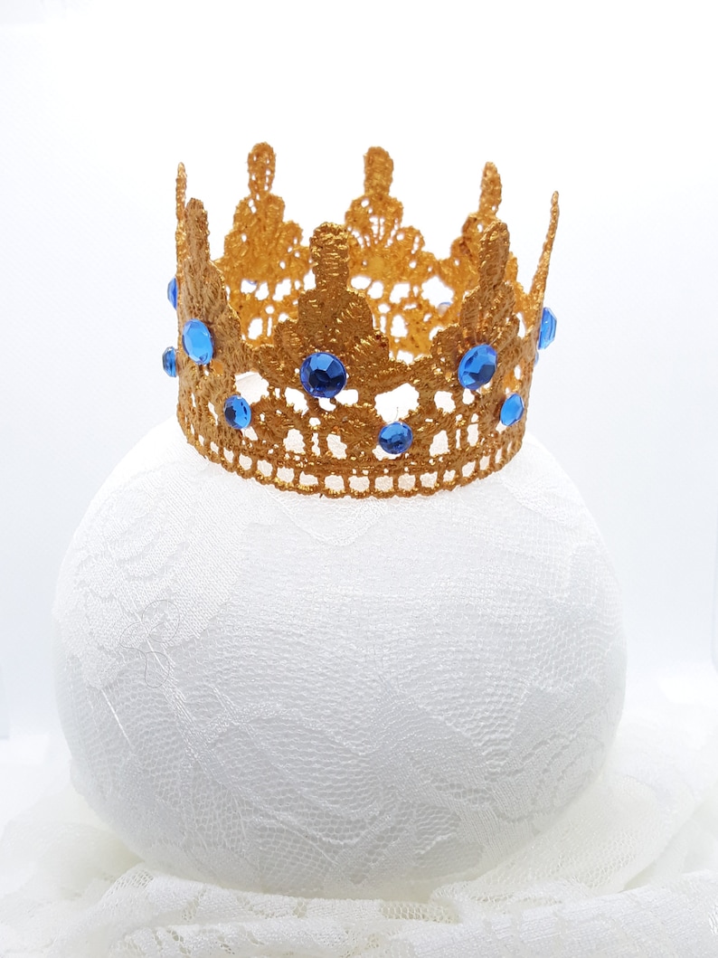 Peut inclure: Une couronne dor&eacute;e avec des pierres bleues, en dentelle, sur un fond blanc.
