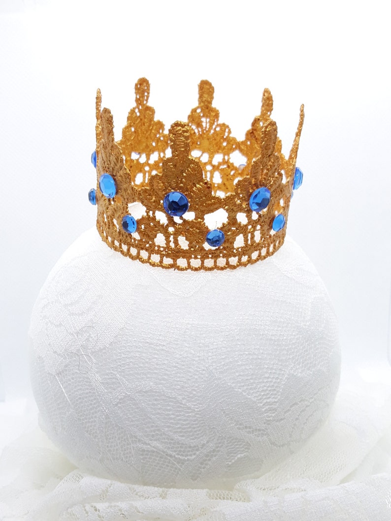 Peut inclure: Une couronne dor&eacute;e avec des pierres bleues, en dentelle, sur un fond blanc.