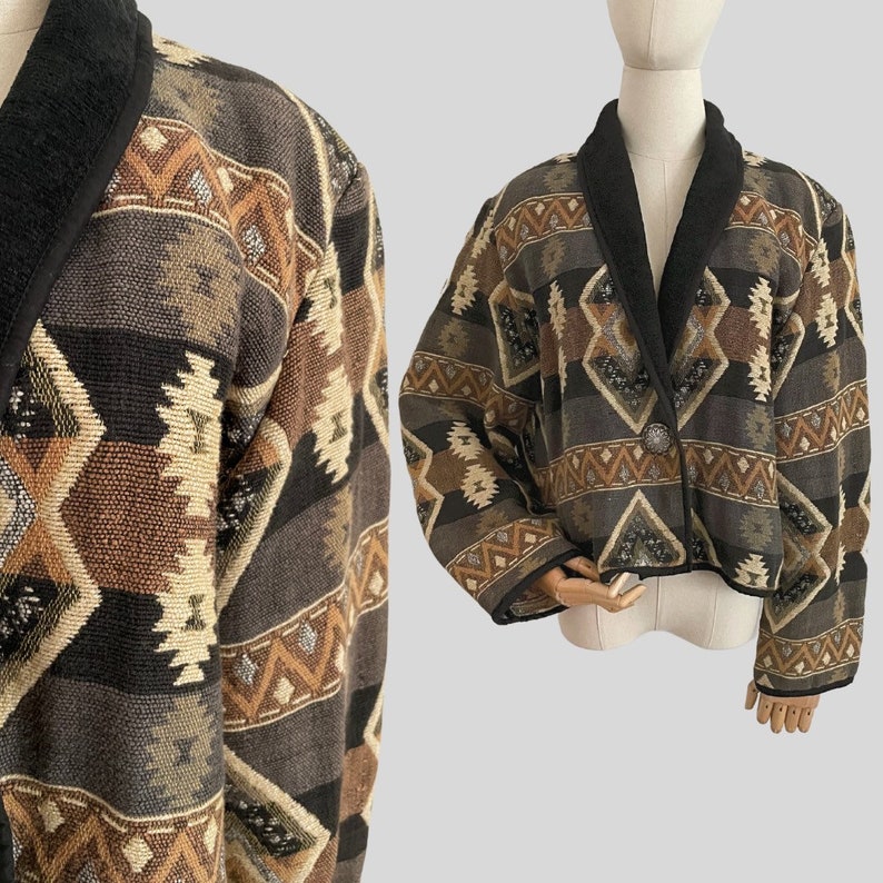 May include: A cropped jacket with a geometric pattern in shades of brown, black, and beige. The jacket has a black collar and trim, and a single button closure. The fabric appears to be woven.