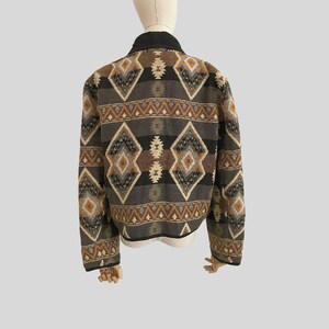 May include: A jacket with a geometric pattern in shades of brown, black, and gray. The jacket has a black collar and trim. The pattern features diamond and zigzag shapes, creating a Southwestern or tribal aesthetic.