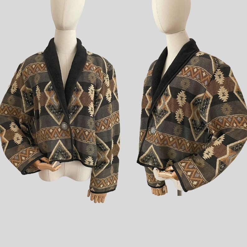 May include: A cropped jacket with a geometric pattern in shades of brown, gray, and beige. The jacket has a black collar and a single button closure. The jacket is displayed on a mannequin.