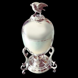May include: Silver egg-shaped warmer with a bird finial on a stand with a burner.