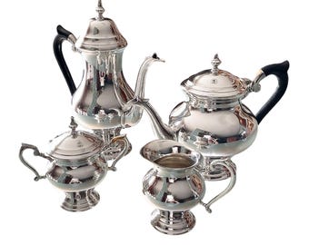 May include: A silver tea set with a teapot, creamer, sugar bowl, and a matching design. The set has black handles and a polished finish.