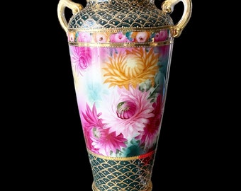 May include: A vintage porcelain vase with a green and gold floral pattern. The vase has two handles and a scalloped rim.