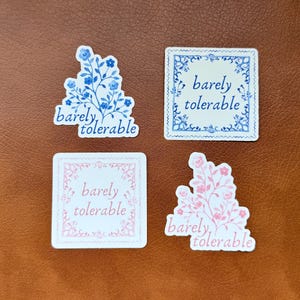 May include: Four stickers with the text "barely tolerable" in a blue and white floral design and a pink and white floral design. Two of the stickers have a square frame with a floral design.