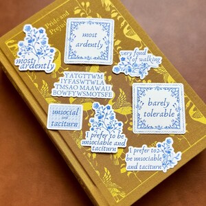 May include: A set of eight blue and white floral stickers with various phrases, including "most ardently", "very fond of walking", "barely tolerable", and "unsocial and taciturn".