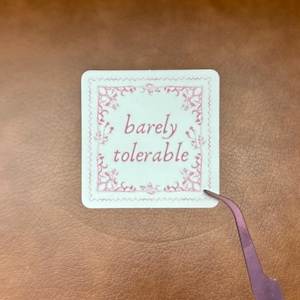 May include: White sticker with a pink ornate border and the text "barely tolerable" in pink lettering.