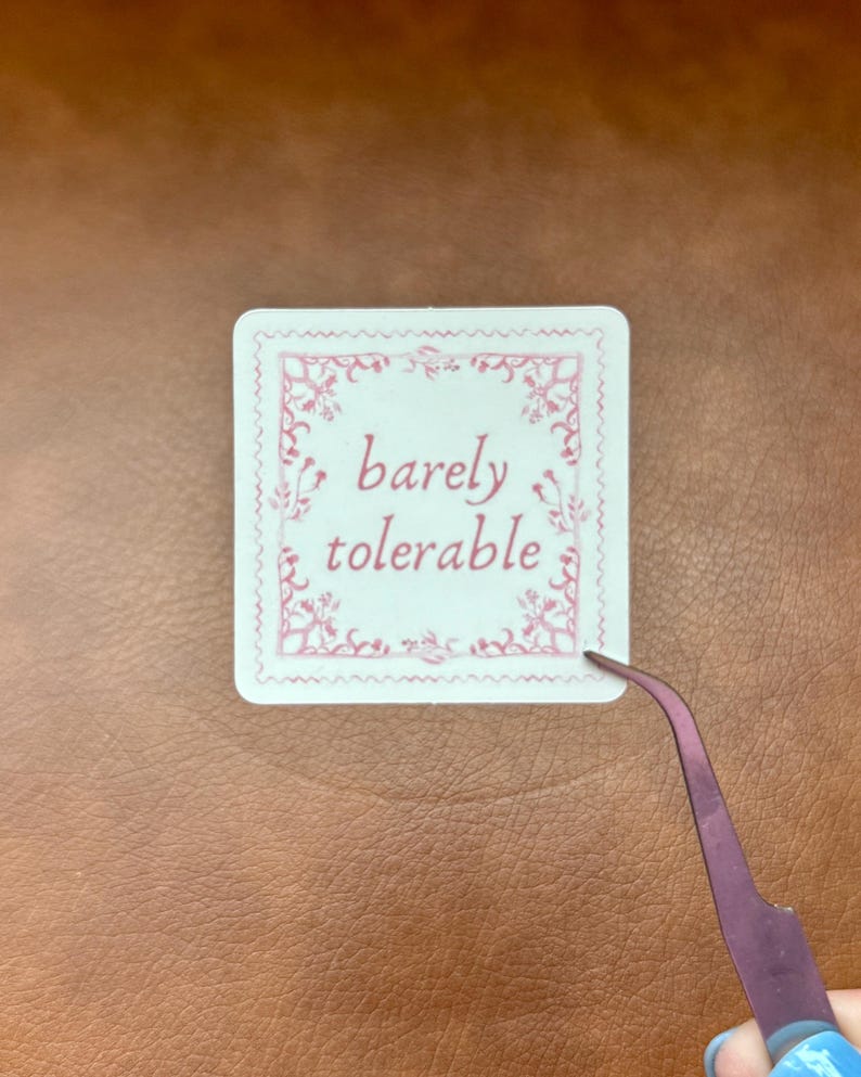 May include: White sticker with a pink ornate border and the text "barely tolerable" in pink lettering.