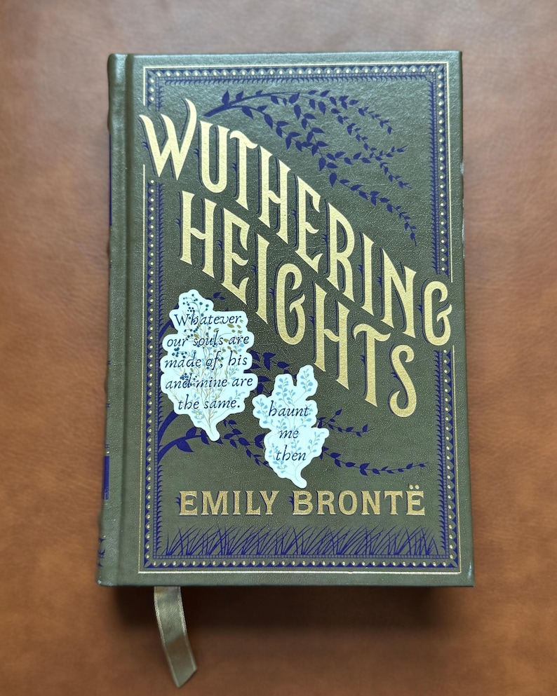 K&ouml;nnte beinhalten: Ein gebundenes Buch mit dem Titel "Wuthering Heights" von Emily Bront&euml;. Das Cover ist olivgr&uuml;n mit goldfarbenen Buchstaben und dunkelblauen dekorativen Elementen. Das Buch hat ein Leseband und Zitat-Aufkleber.