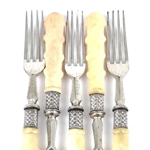 May include: Set of five silver forks with ivory handles. The forks have a decorative design on the handle and are in good condition.