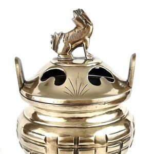 Puede incluir: Un quemador de incienso de latón con un remate de dragón en la tapa. El quemador tiene un patrón tejido en el cuerpo y tres patas.