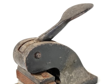 May include: A vintage metal hand stamp with a black finish and a wooden handle. The stamp has a rectangular base and a lever that is used to press the stamp down.