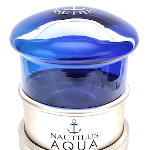 May include: A silver and blue glass bottle stopper with an anchor and the text "NAUTILUS AQUA".