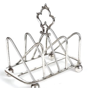 May include: Silver plated toast rack with a decorative top and four ball feet.