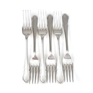 May include: Six silver forks with ornate handles, arranged in a row on a white background.