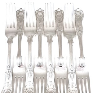Peut inclure: Huit fourchettes argentées disposées verticalement. Chaque fourchette présente un motif orné sur le manche, avec des éléments floraux et en forme de coquillage. Les dents sont fines et uniformes. Elles sont présentées sur fond blanc.