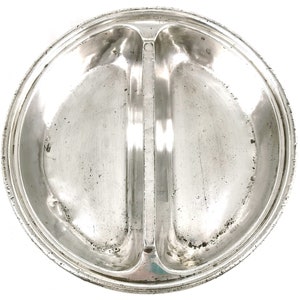 Puede incluir: Un plato de servir de plata con dos secciones divididas. El plato tiene un borde elevado y un borde decorativo.