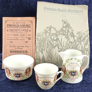 May include: Three white ceramic teacups with gold trim and a floral design. The cups feature a printed image of a coat of arms with the text "Preston Guild Merchant" and "Royal Charter of Henry II, 1180".