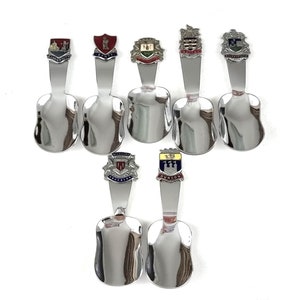 May include: Set of seven silver souvenir spoons with different coloured enamel crests. Each spoon features a different city crest, including Scarborough, Whitby, Dundee, and Aberdeen.