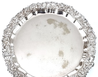 May include: A silver serving tray with a decorative, ornate border. The tray is round and has a smooth, polished surface.