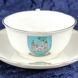 May include: White teacup and saucer with a gold trim. The saucer has a gold crest with the words "Scarborough" and "Honorum Tuta" in a banner.