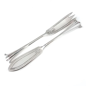May include: Two silver serving utensils on a white background. One is a butter knife with a pointed end and a decorative floral design. The other is a fork with three tines and a similar floral design.