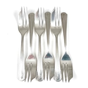 May include: Six vintage silver forks arranged on a white background. The forks have a classic design with three tines and decorative detailing on the handles. The silver color is bright and reflective, suggesting they are well-maintained.