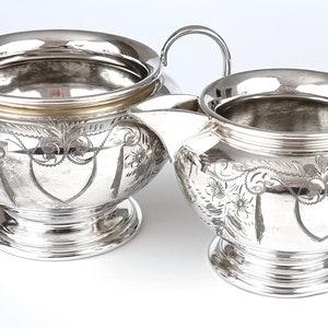 May include: A silver sugar bowl and creamer set with ornate floral designs. The pieces have a polished finish and a classic design.