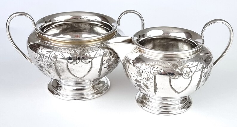 May include: A silver sugar bowl and creamer set with ornate floral designs. The pieces have a polished finish and a classic design.