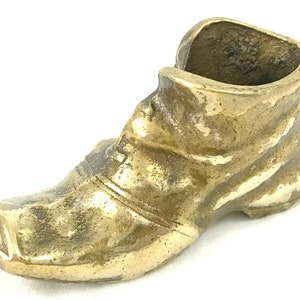 May include: A gold-colored metal shoe-shaped trinket with a worn finish. The shoe is open at the top and could be used as a small decorative container.