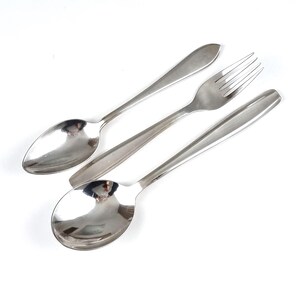 Könnte beinhalten: Ein Set aus Edelstahlbesteck, bestehend aus zwei Löffeln und einer Gabel, angeordnet auf einer weißen Oberfläche. Die Löffel haben ovale Laffen und lange Griffe. Die Gabel hat vier Zinken. Das Besteck ist reflektierend, mit poliertem Finish.